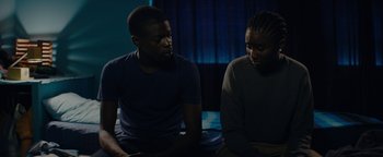 Movie still from “Girlhood” (2014), directed by Céline Sciamma – A man and a woman sitting next to each other on a bed; Medium shot, High angle