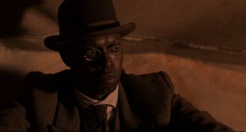 Movie still from “Glory” (1989), directed by Edward Zwick – A man wearing a suit and hat and glasses; Close Up shot, Over the shoulder angle