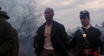 Movie still from “Glory” (1989), directed by Edward Zwick – A man in a black coat and brown pants walking; Medium shot, Over the shoulder angle