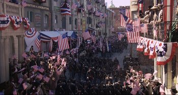 Movie still from “Glory” (1989), directed by Edward Zwick – A crowd of people walking down a street with american flags; Extreme Wide shot, High angle