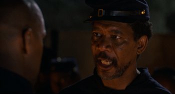 Movie still from “Glory” (1989), directed by Edward Zwick – An older man wearing a black hat and a black shirt; Close Up shot, Over the shoulder angle
