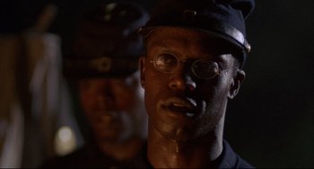 Movie still from “Glory” (1989), directed by Edward Zwick – A man wearing a hat and glasses is looking at the camera; Close Up shot, Low angle