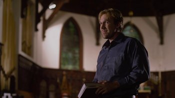 Movie still from “God's Not Dead” (2014), directed by Harold Cronk – A man standing in a room holding a book; Medium shot, Low angle
