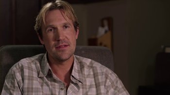 Movie still from “God's Not Dead” (2014), directed by Harold Cronk – A person sitting in a chair wearing a plaid shirt; Close Up shot, Over the shoulder angle