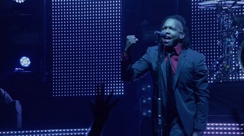 Movie still from “God's Not Dead” (2014), directed by Harold Cronk – A man in a black suit and a red shirt is singing into a microphone; Medium shot, Low angle