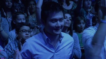 Movie still from “God's Not Dead” (2014), directed by Harold Cronk – A group of people watching a man in a blue shirt; Medium shot, Over the shoulder angle