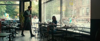 Movie still from “How to Be Single” (2016), directed by Christian Ditter – A woman sitting at a table in front of a window; Wide shot, Over the shoulder angle