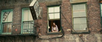 Movie still from “How to Be Single” (2016), directed by Christian Ditter – A woman looking out of a window on the side of a brick building; Wide shot, High angle