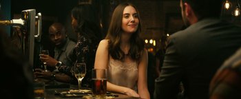 Movie still from “How to Be Single” (2016), directed by Christian Ditter – A beautiful young lady sitting at a table with a glass of wine in front of her; Medium shot, Over the shoulder angle