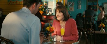 Movie still from “How to Be Single” (2016), directed by Christian Ditter – A woman sitting at a table in front of a glass of champagne; Medium shot, Over the shoulder angle