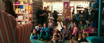 Movie still from “How to Be Single” (2016), directed by Christian Ditter – A group of people sitting in a room with books; Wide shot, High angle