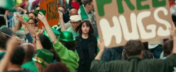 Movie still from “How to Be Single” (2016), directed by Christian Ditter – A woman in a crowd of people wearing green hats and holding signs; Medium shot, Over the shoulder angle
