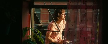 Movie still from “How to Be Single” (2016), directed by Christian Ditter – A woman sitting on top of a chair next to a window; Medium shot, Over the shoulder angle