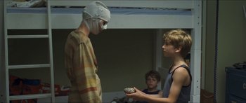 Movie still from “Goodnight Mommy” (2014), directed by Severin Fiala – A man wearing bandages is holding a bowl of food; Medium shot, Over the shoulder angle