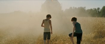Movie still from “Goodnight Mommy” (2014), directed by Severin Fiala – Two young people are standing in a field near a building; Wide shot, Low angle