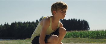 Movie still from “Goodnight Mommy” (2014), directed by Severin Fiala – A young man squatting on the ground in the grass; Medium shot, High angle