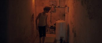 Movie still from “Goodnight Mommy” (2014), directed by Severin Fiala – A woman standing next to a water tank in a bathroom; Wide shot, High angle