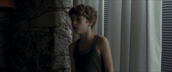 Movie still from “Goodnight Mommy” (2014), directed by Severin Fiala – A young boy standing in front of a stone wall; Medium shot, Over the shoulder angle