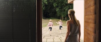 Movie still from “Goodnight Mommy” (2014), directed by Severin Fiala – Two young children running in a courtyard with a woman looking on; Wide shot, Over the shoulder angle