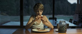 Movie still from “Goodnight Mommy” (2014), directed by Severin Fiala – A young boy sitting at a table eating a piece of pizza; Medium shot, Over the shoulder angle