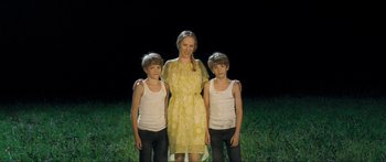 Movie still from “Goodnight Mommy” (2014), directed by Severin Fiala – A woman standing between two young boys in a field; Medium shot, High angle