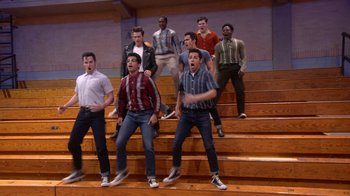 Movie still from “Grease Live!” (2016), directed by Thomas Kail – A group of young men standing on top of a wooden staircase; Wide shot, Low angle