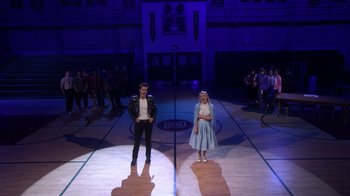 Movie still from “Grease Live!” (2016), directed by Thomas Kail – A couple of people that are standing in a room; Wide shot, High angle