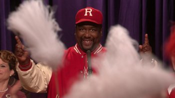 Movie still from “Grease Live!” (2016), directed by Thomas Kail – A man in a red baseball cap and a microphone; Close Up shot, Low angle