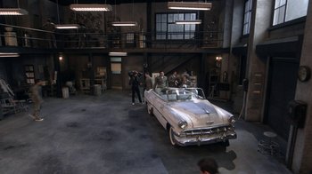 Movie still from “Grease Live!” (2016), directed by Thomas Kail – An old car is parked in a garage with people standing around it; Extreme Wide shot, High angle