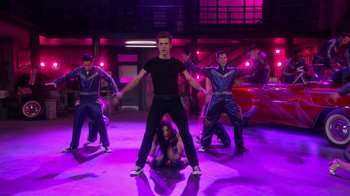 Movie still from “Grease Live!” (2016), directed by Thomas Kail – A group of men and women performing on a stage; Wide shot, Low angle