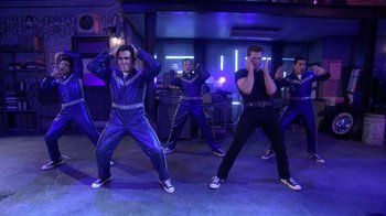 Movie still from “Grease Live!” (2016), directed by Thomas Kail – A group of men in blue and black outfits doing a dance move; Wide shot, Low angle
