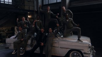 Movie still from “Grease Live!” (2016), directed by Thomas Kail – A group of men standing next to each other on top of an old car; Wide shot, High angle