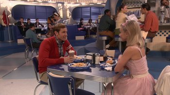 Movie still from “Grease Live!” (2016), directed by Thomas Kail – A man and a woman sitting at a table eating pizza; Wide shot, Over the shoulder angle