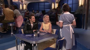 Movie still from “Grease Live!” (2016), directed by Thomas Kail – A man and a woman sitting at a table in front of a waitress; Wide shot, Over the shoulder angle
