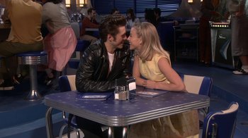 Movie still from “Grease Live!” (2016), directed by Thomas Kail – A man and a woman sitting at a table together; Medium shot, Over the shoulder angle