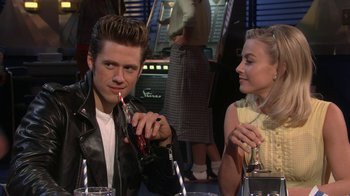 Movie still from “Grease Live!” (2016), directed by Thomas Kail – A man and a woman sitting at a table with drinks; Medium shot, Over the shoulder angle