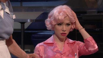 Movie still from “Grease Live!” (2016), directed by Thomas Kail – A woman in a pink wig and a pink shirt; Close Up shot, Over the shoulder angle