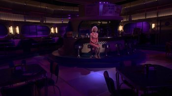 Movie still from “Grease Live!” (2016), directed by Thomas Kail – A woman sitting on a bench in a restaurant; Wide shot, High angle