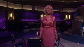 Movie still from “Grease Live!” (2016), directed by Thomas Kail – A woman in a pink dress and pink wig singing; Medium shot, Over the shoulder angle