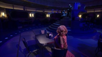 Movie still from “Grease Live!” (2016), directed by Thomas Kail – A woman sitting at a table in front of a stage; Wide shot, Over the shoulder angle