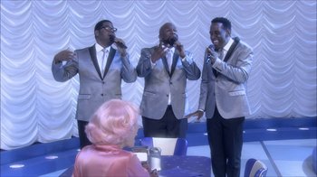 Movie still from “Grease Live!” (2016), directed by Thomas Kail – A group of men singing in front of a woman; Wide shot, Over the shoulder angle