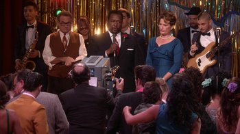 Movie still from “Grease Live!” (2016), directed by Thomas Kail – A group of people standing in front of a microphone; Wide shot, Over the shoulder angle