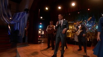Movie still from “Grease Live!” (2016), directed by Thomas Kail – A group of men standing on a stage with microphones; Wide shot, Over the shoulder angle