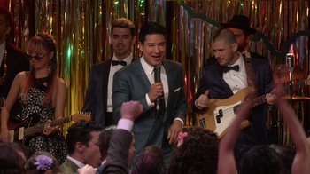 Movie still from “Grease Live!” (2016), directed by Thomas Kail – A group of men in suits singing into microphones in front of a crowd; Medium shot, Over the shoulder angle