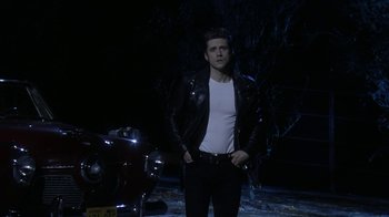 Movie still from “Grease Live!” (2016), directed by Thomas Kail – A man in a leather jacket standing next to a motorcycle; Medium shot, Low angle