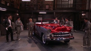 Movie still from “Grease Live!” (2016), directed by Thomas Kail – A group of people standing next to an antique car; Extreme Wide shot, High angle