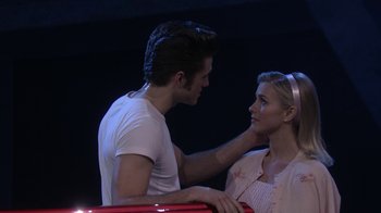 Movie still from “Grease Live!” (2016), directed by Thomas Kail – A man and a woman are touching each other's hair; Medium shot, Over the shoulder angle