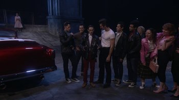 Movie still from “Grease Live!” (2016), directed by Thomas Kail – A group of young men standing next to each other in front of a red car; Wide shot, High angle
