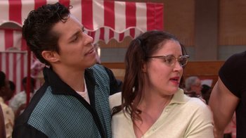 Movie still from “Grease Live!” (2016), directed by Thomas Kail – A man standing next to a woman wearing glasses; Medium shot, Over the shoulder angle