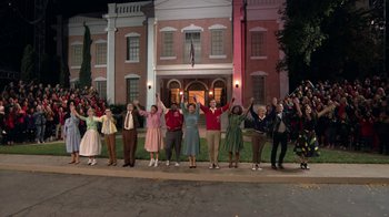 Movie still from “Grease Live!” (2016), directed by Thomas Kail – A group of people standing in front of a large building; Extreme Wide shot, High angle